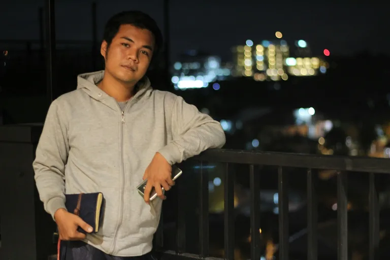 Ibrahim Anwar berdiri di balkon pada malam hari sambil memegang jurnal kulit jahitan tangan