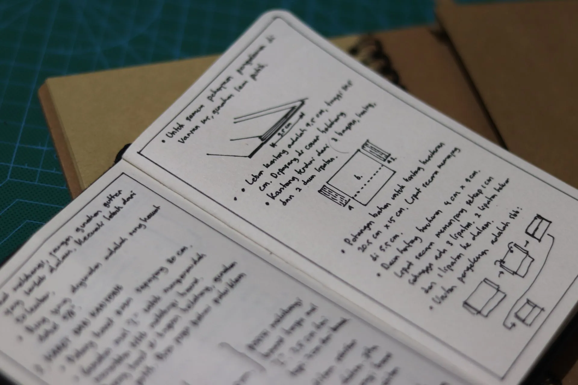 Buku catatan terbuka berisi instruksi dan diagram tulisan tangan untuk pembuatan produk kulit, di atas cutting mat di samping jurnal-jurnal kulit lainnya