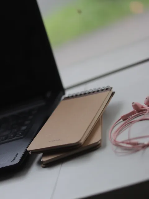 Beberapa buku catatan berwarna krem diletakkan di samping laptop di atas meja kerja, menunjukkan kegunaannya dalam lingkungan profesional atau akademis.