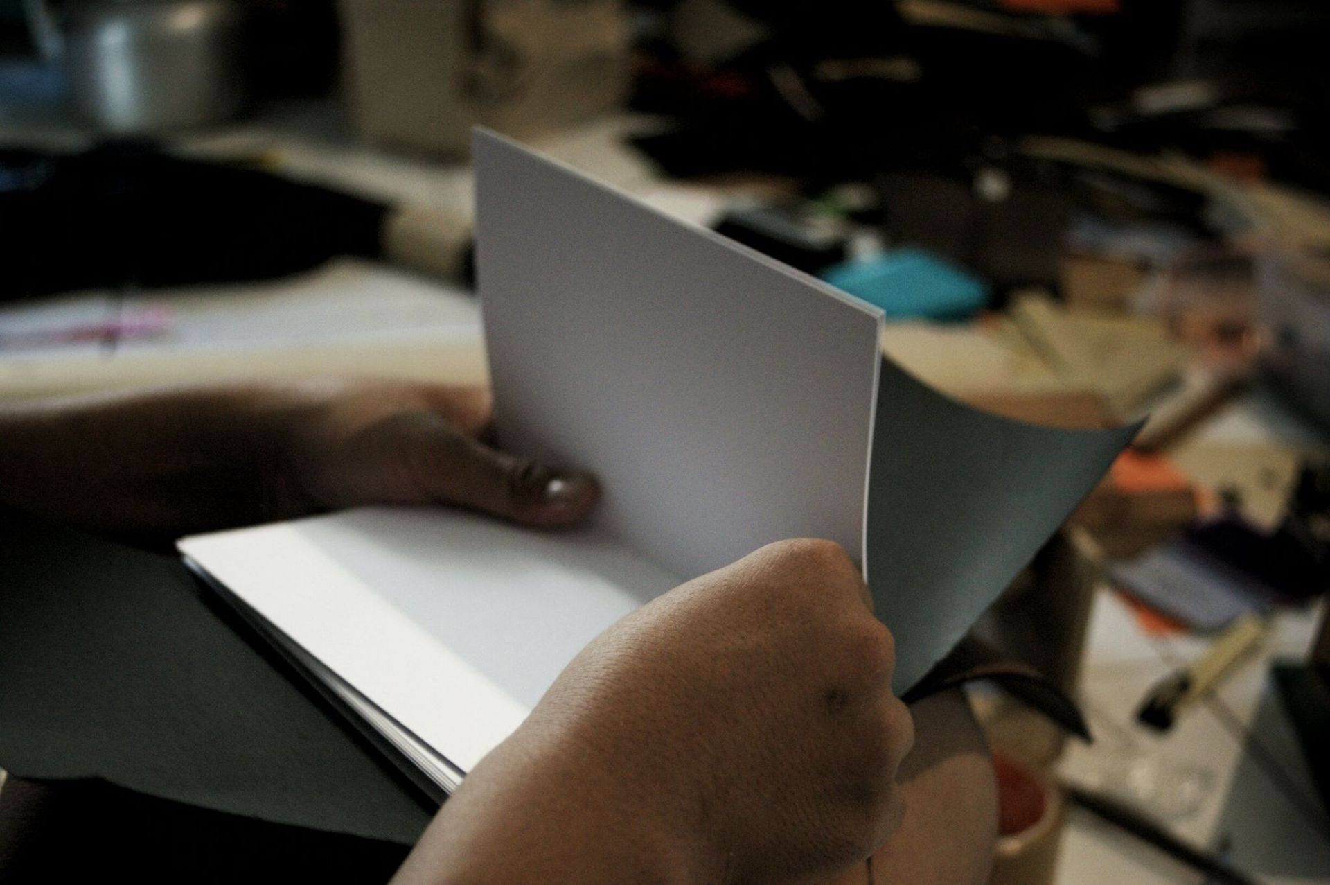 Tangan seorang pengrajin sedang membuka dan merapikan lembaran kertas putih di dalam sebuah buku yang sedang dalam proses penjilidan.
