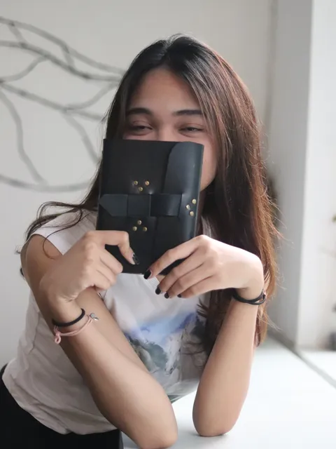 Seorang gadis sedang menulis di jurnal kulit hitam, menunjukkan penggunaan personal yang praktis.