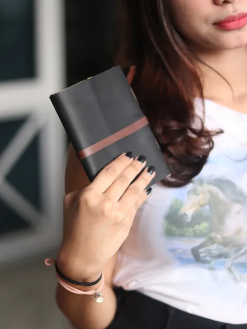 Seorang wanita memegang jurnal kulit hitam yang kokoh, melambangkan durabilitas dan keandalan.