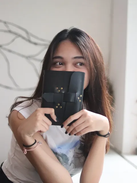 Wanita memegang buku catatan kulit hitam yang dipersonalisasi, menandakan kustomisasi dan kualitas premium.