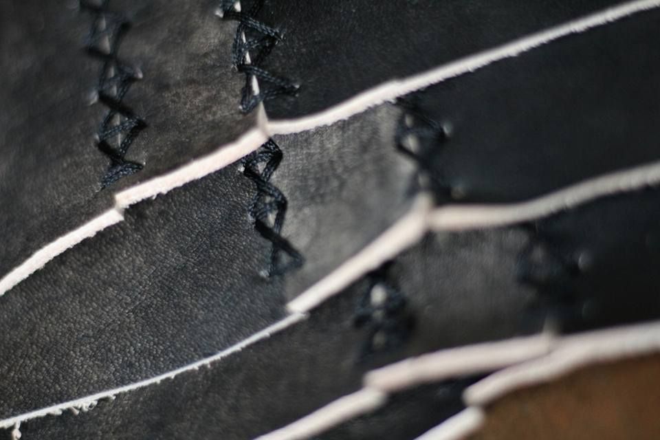 Tampilan close-up dari jahitan silang dengan benang hitam pada beberapa potong kulit hitam, menunjukkan detail dan presisi.