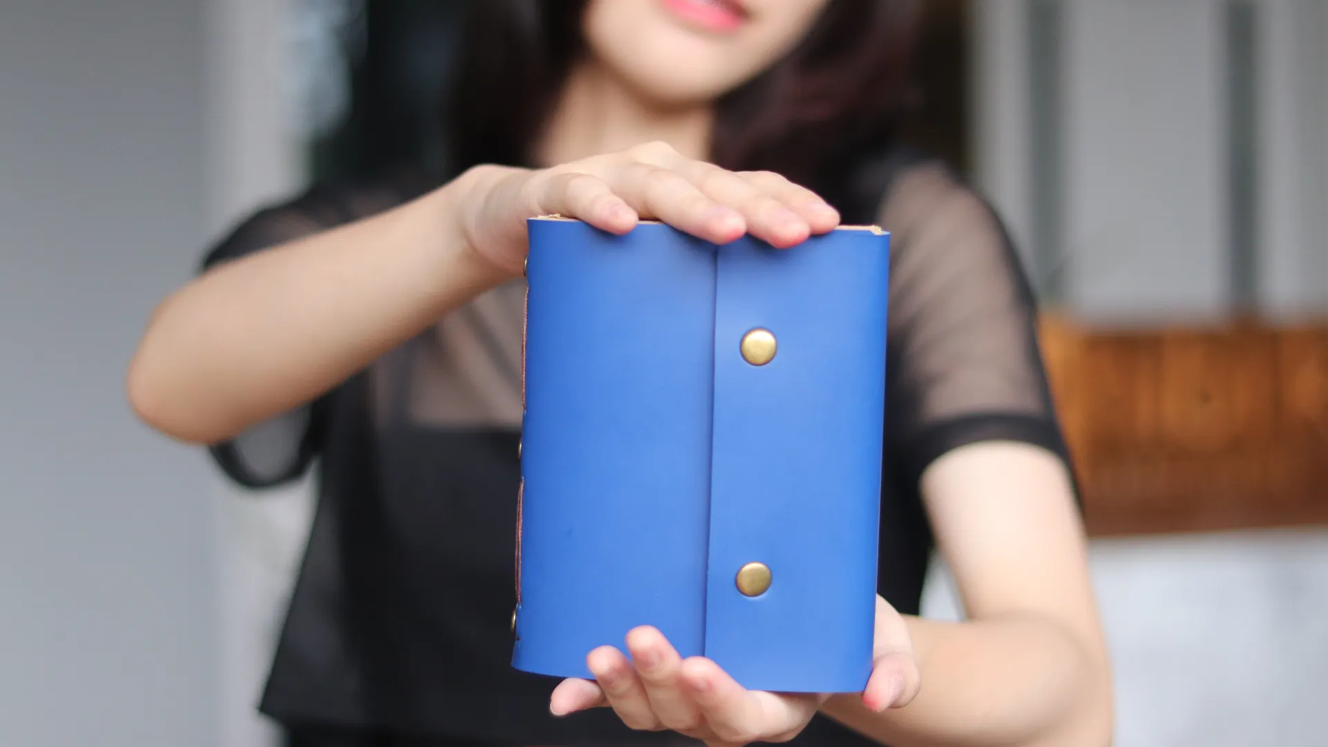 Seorang wanita profesional memegang agenda kulit eksklusif berwarna biru, menunjukkan status dan keanggunan.