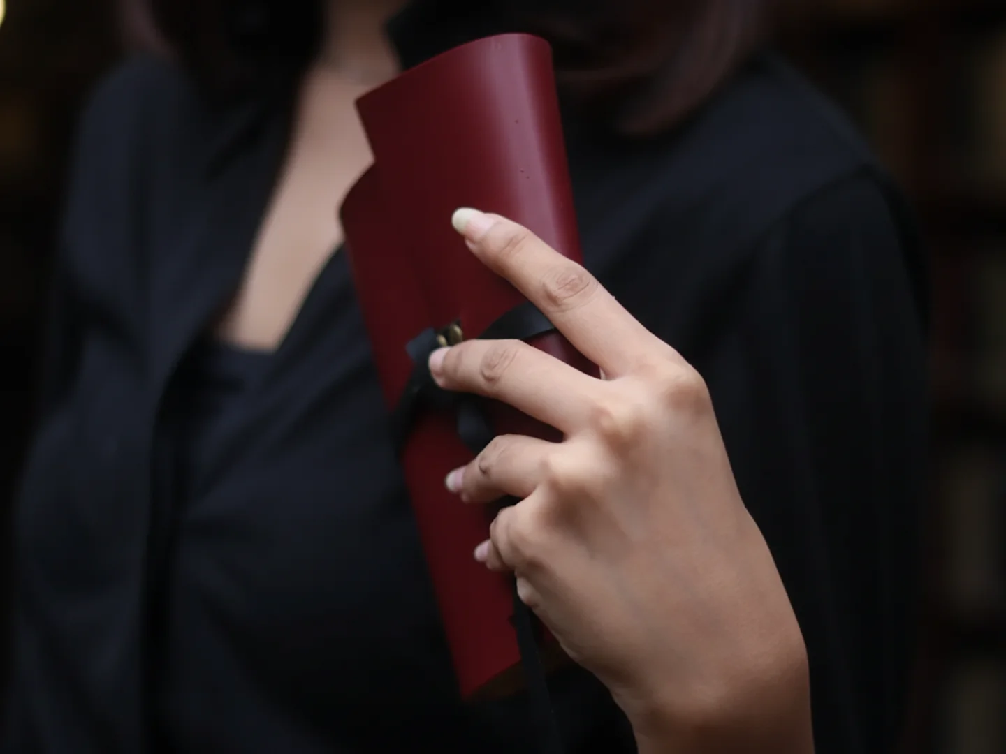 Tangan memegang sebuah jurnal kulit berwarna burgundy, melambangkan hadiah yang dipilih dengan cermat, personal, dan berkualitas tinggi.