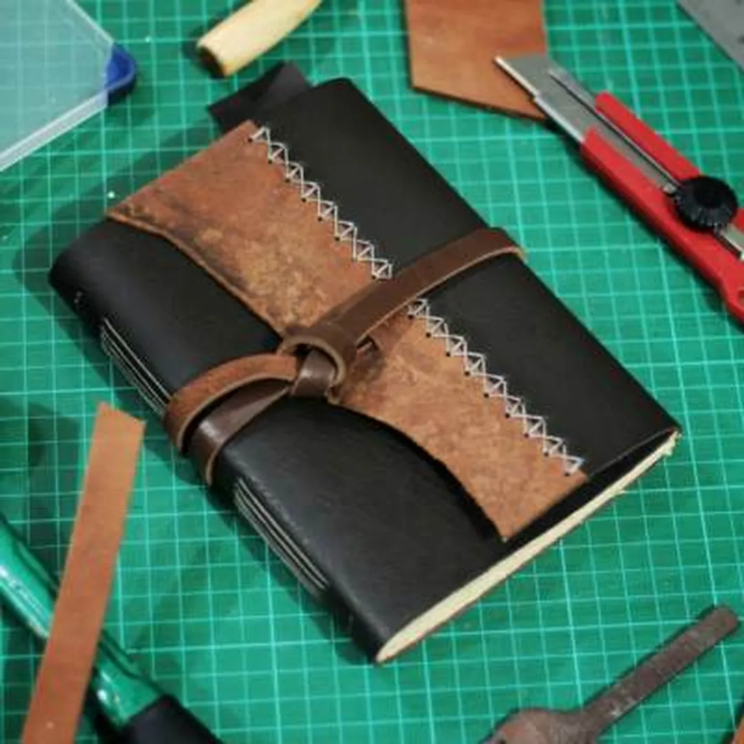 Sebuah jurnal kulit buatan tangan dengan jahitan yang terlihat, menyoroti aspek kerajinan dan keserbagunaan material kulit.