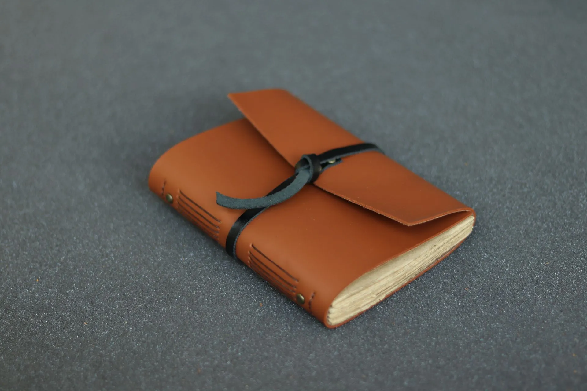 Jurnal kulit Basic berwarna coklat tua terbaring di atas permukaan abu-abu, dengan tali pengikat yang terikat rapi.