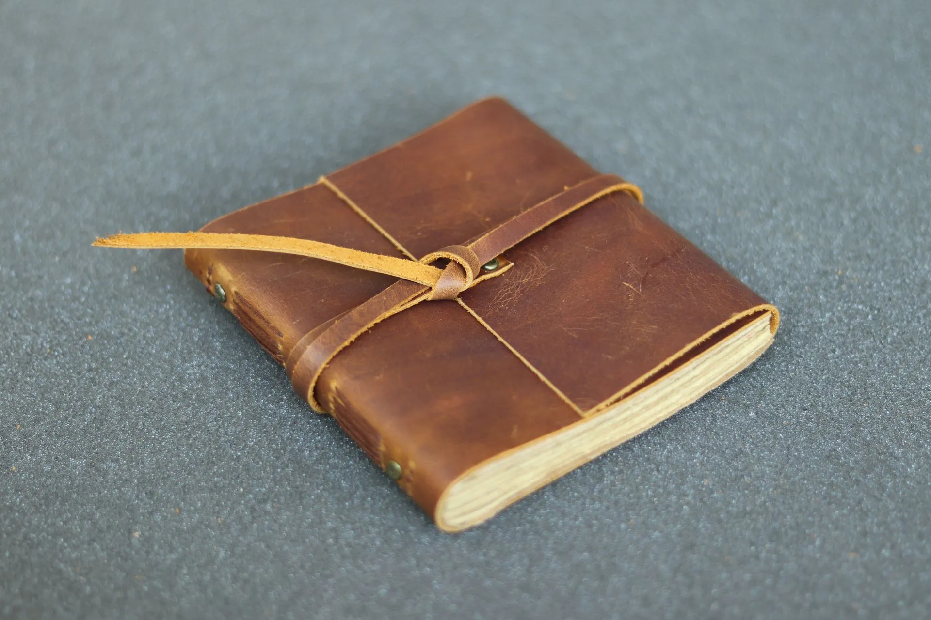 Jurnal kulit Hibrkraft Basic berwarna coklat yang terlihat tangguh dan klasik tergeletak di atas meja kayu.