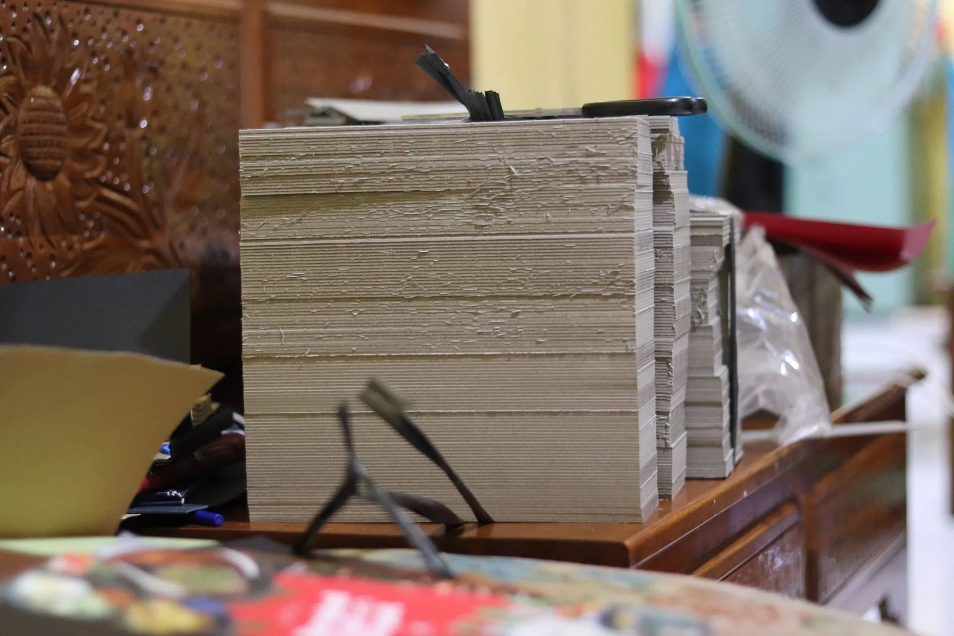 Tumpukan tebal karton atau kayu lapis yang dipotong rapi, siap untuk digunakan dalam proses produksi di workshop.