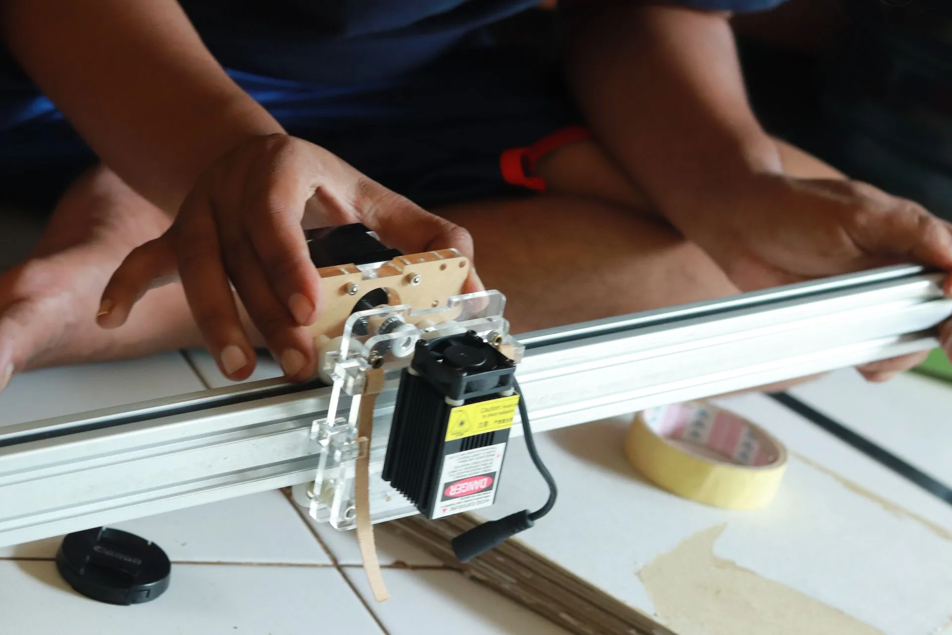 Close-up modul laser engraver non-CO2 yang dipasang pada rel aluminium, fokus pada kepala laser yang siap untuk proses grafir.