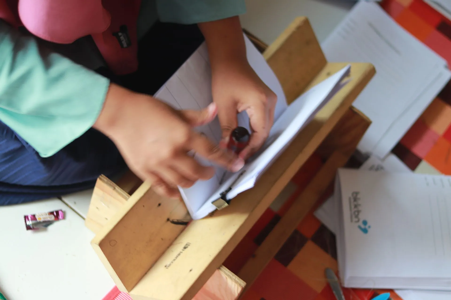 Tangan pengrajin memegang pelubang tepat di atas kertas terlipat yang bertumpu pada cradle kayu buatan sendiri.