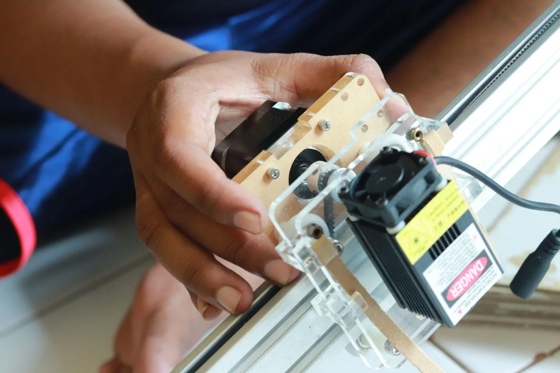 Tangan seseorang sedang mengatur modul laser engraver non-CO2 yang dipasang pada rel, menunjukkan proses penyiapan untuk personalisasi produk.