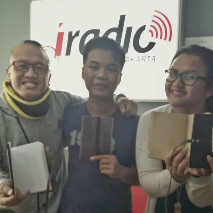 Tim Hibrkraft bersama penyiar di studio iRadio Jakarta, semuanya tersenyum sambil memegang jurnal kulit.