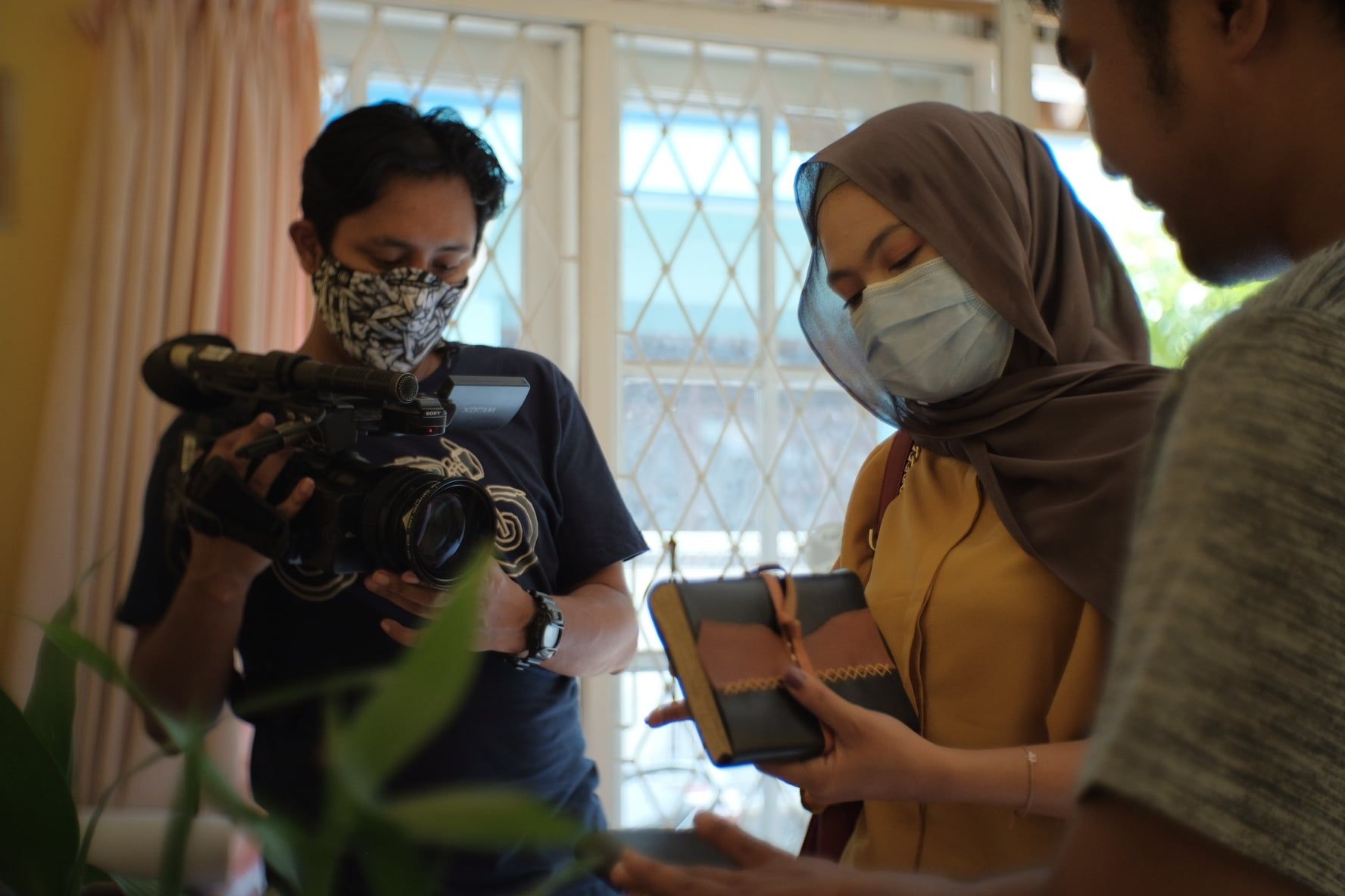 Fokus pada jurnal kulit Hibrkraft yang dipegang oleh seorang wanita berhijab, direkam oleh kamera profesional.