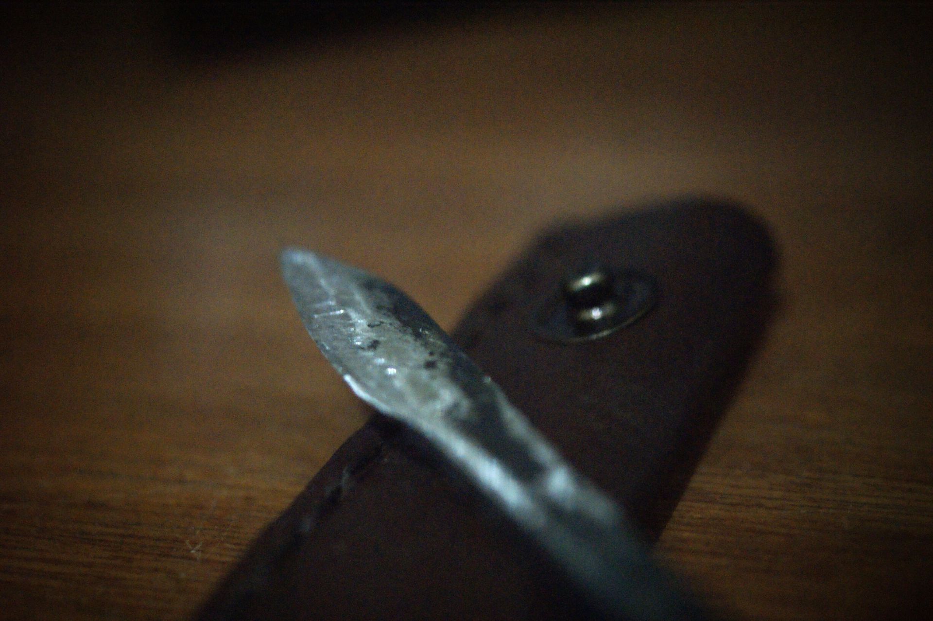 Pisau seset kulit buatan tangan tergeletak di atas meja kayu di sebelah sarung kulitnya yang berwarna coklat tua.