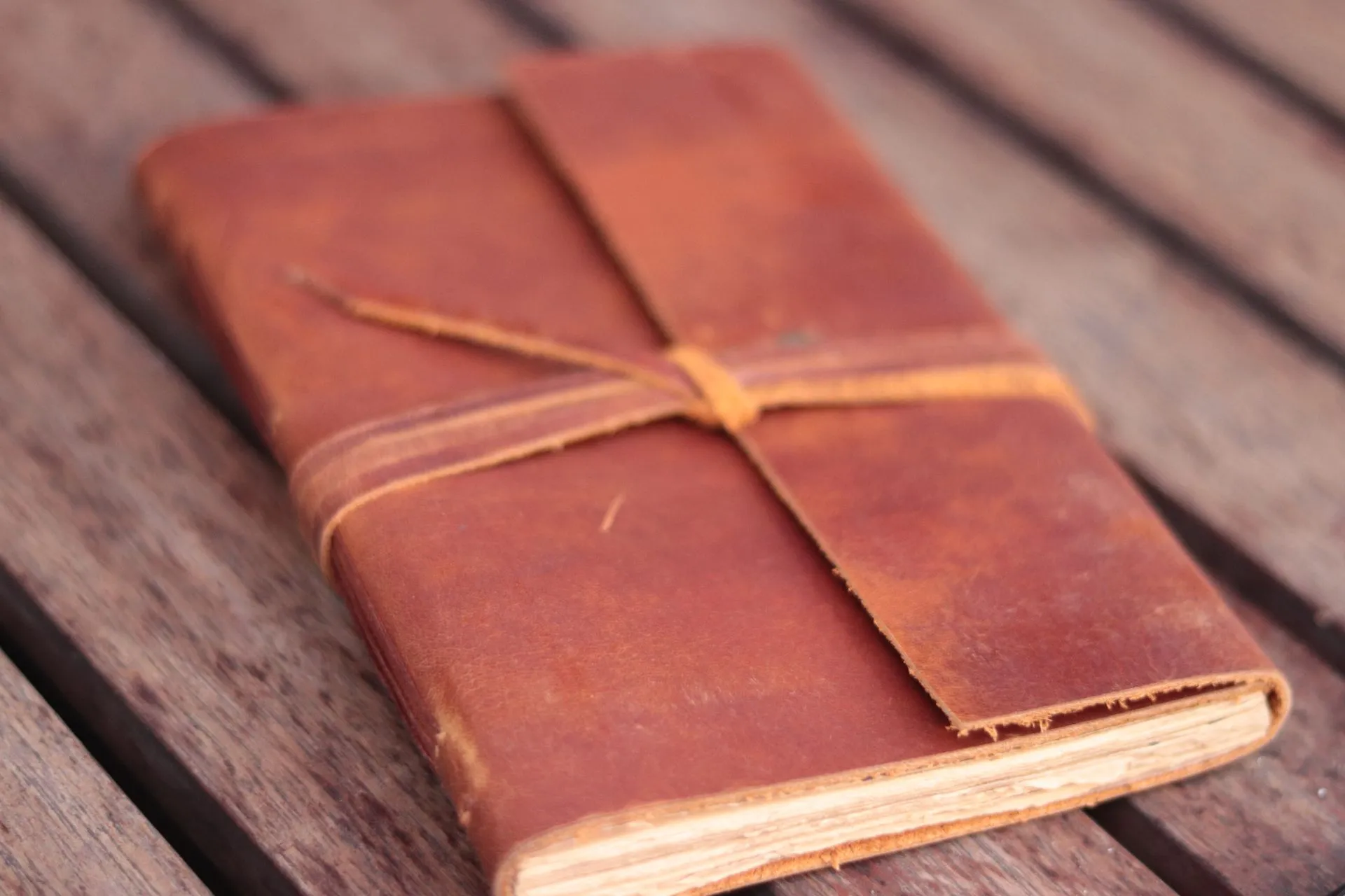 Jurnal kulit Hibrkraft varian Basic berwarna tan berdiri tegak dengan latar belakang hitam, menunjukkan detail tali pengikatnya.