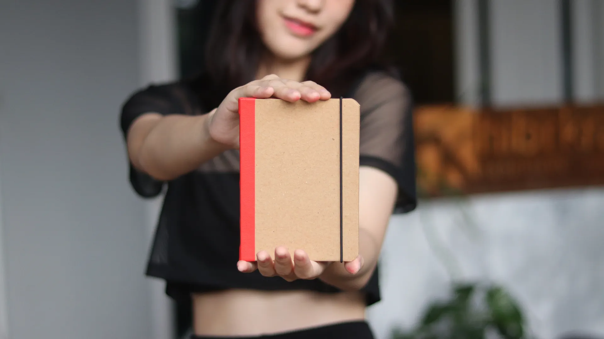 Seorang wanita menunjukkan sebuah custom notebook dengan sampul kraft dan punggung buku berwarna merah cerah.