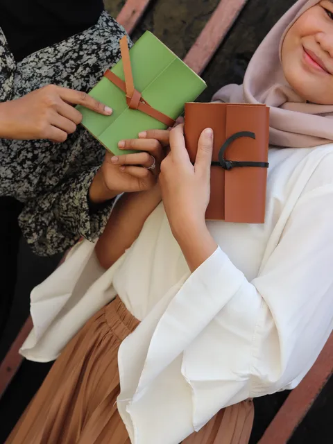 Wanita memegang jurnal kulit cokelat yang elegan