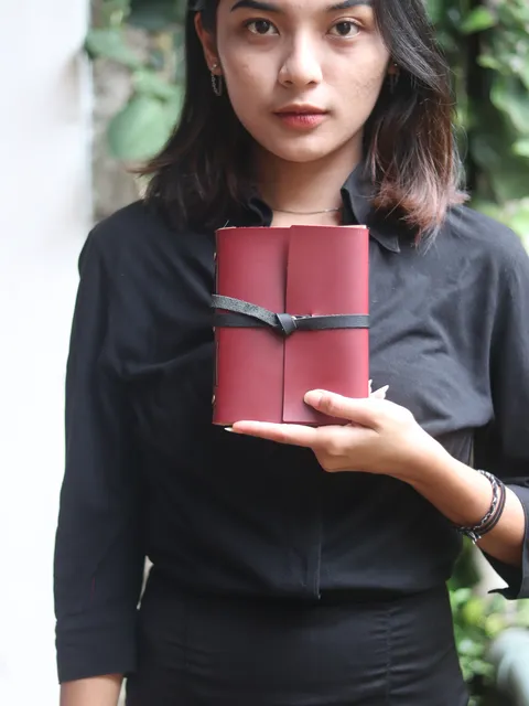 Buku catatan kulit berwarna merah marun, menyoroti keindahan dan tekstur material premium.