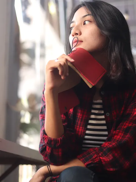 Tangan seorang wanita dengan lembut memegang custom notebook berwarna merah, menunjukkan tindakan perawatan dan kepemilikan.
