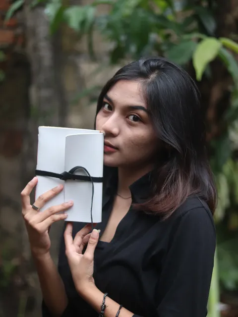 Seorang wanita dengan kemeja hitam memegang jurnal kulit putih bersih, menonjolkan desainnya yang klasik dan abadi.