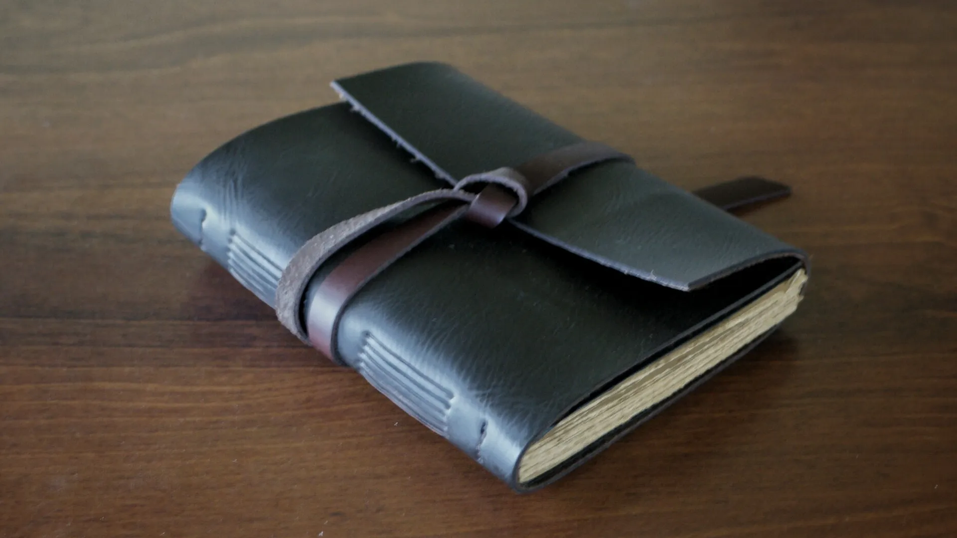 Jurnal kulit hitam diletakkan di atas permukaan kayu, menunjukkan desainnya yang klasik dan profesional untuk musisi.