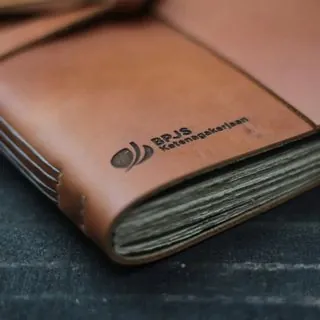 Notebook kulit dengan deboss logo BPJS Ketenagakerjaan di dekat punggung sampul, contoh notebook custom untuk korporat