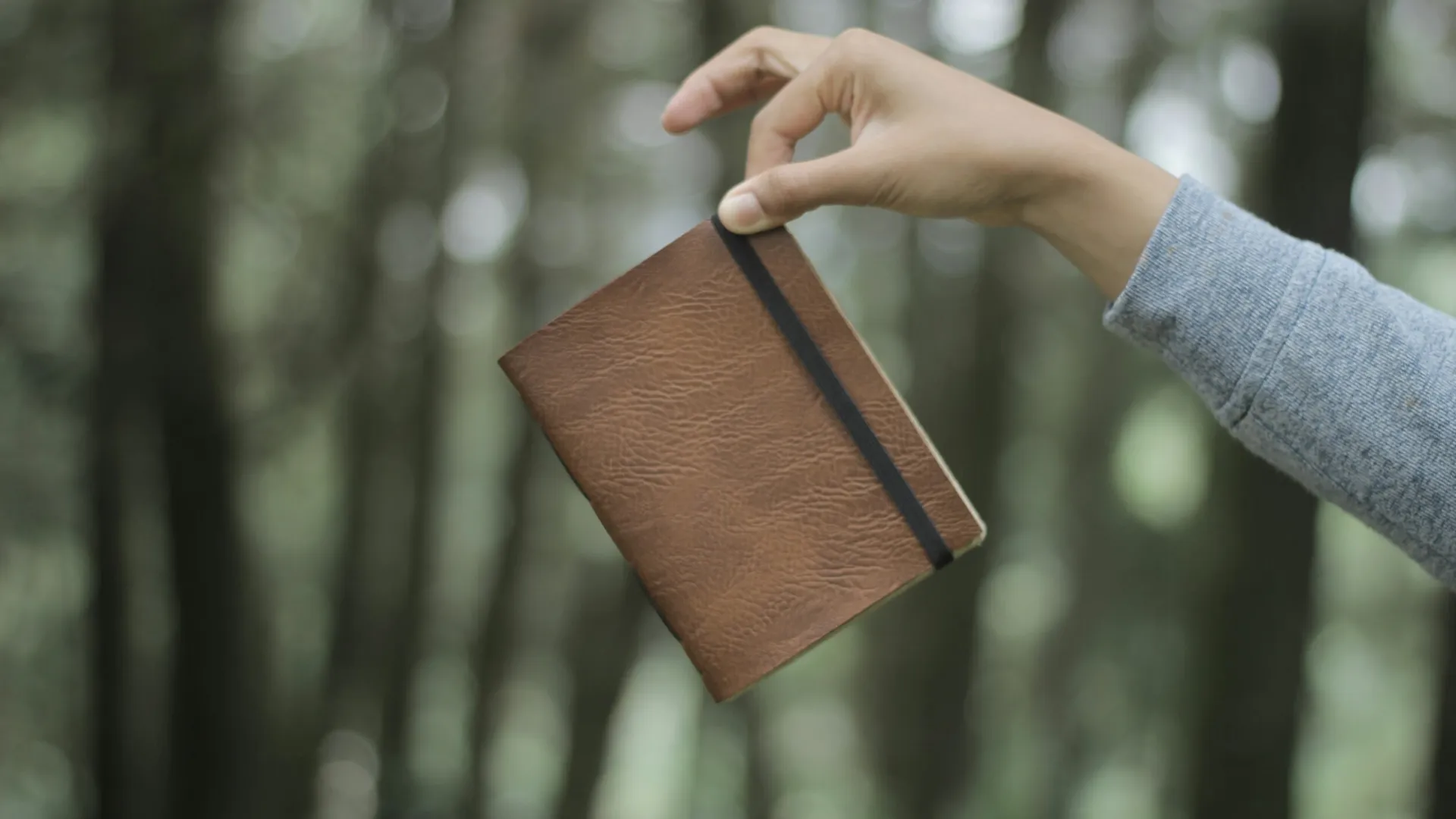 Tangan seseorang memegang jurnal kulit coklat dengan erat, melambangkan hubungan personal seorang penyair dengan bukunya.