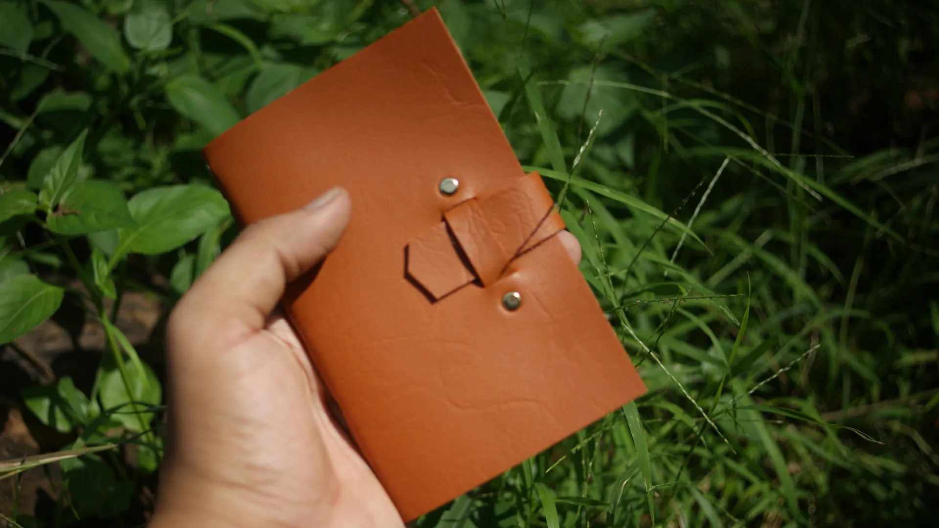 Seseorang memegang jurnal kulit coklat dengan santai, menunjukkan portabilitas dan kenyamanannya.