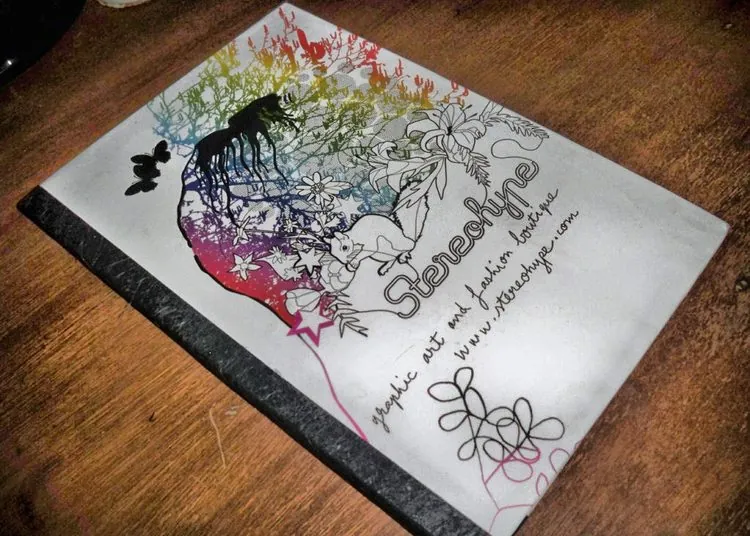 Journal with a rainbow-coloured illustration, a silhouette figure, floral branches, a squirrel and a butterfly, printed with a boutique’s name and web address