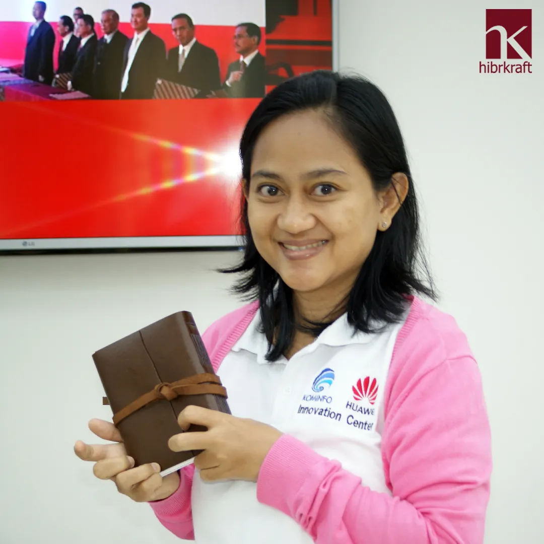 A woman in a pink cardigan and white shirt holding a classic brown leather wrap journal gently with both hands