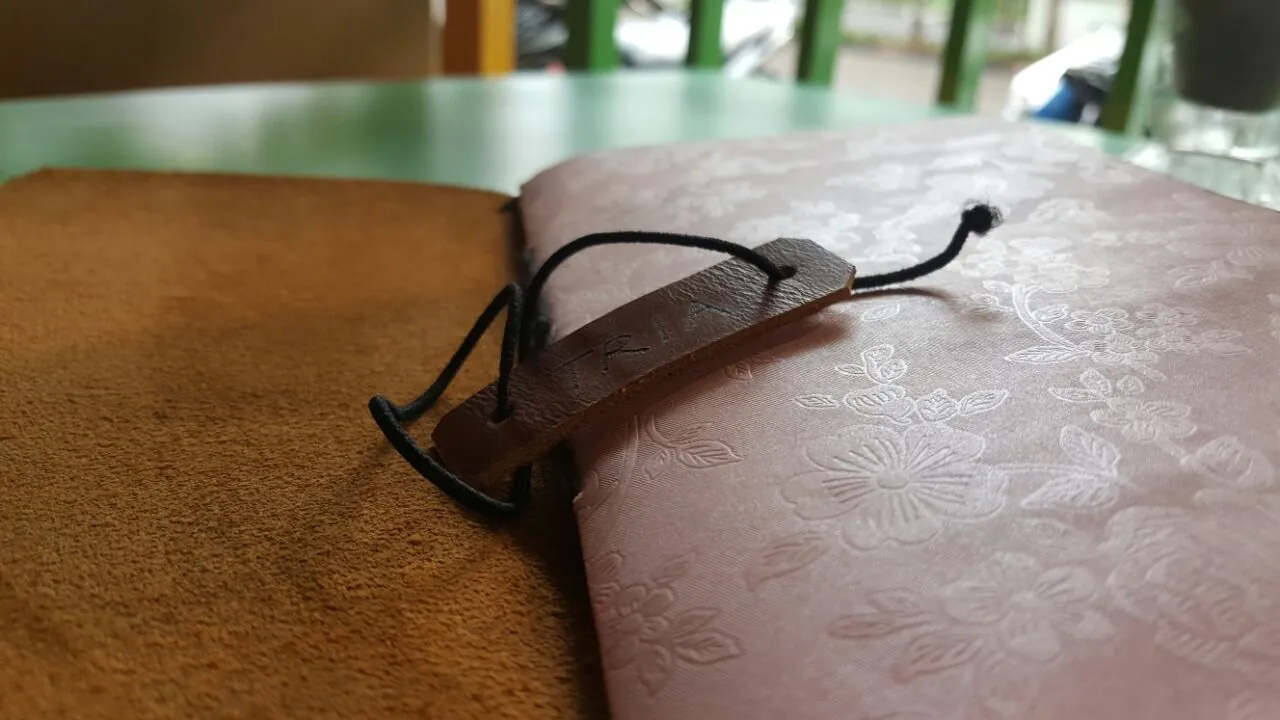 Close up of a pink floral notebook bound with a black string and a small brown leather tag stamped with the name TRIA