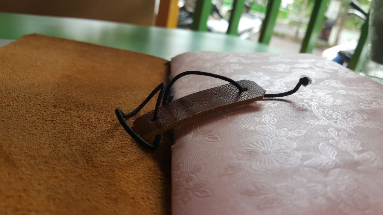 The finished leather travel journal cover in rich brown with the TRIA tag tied around it