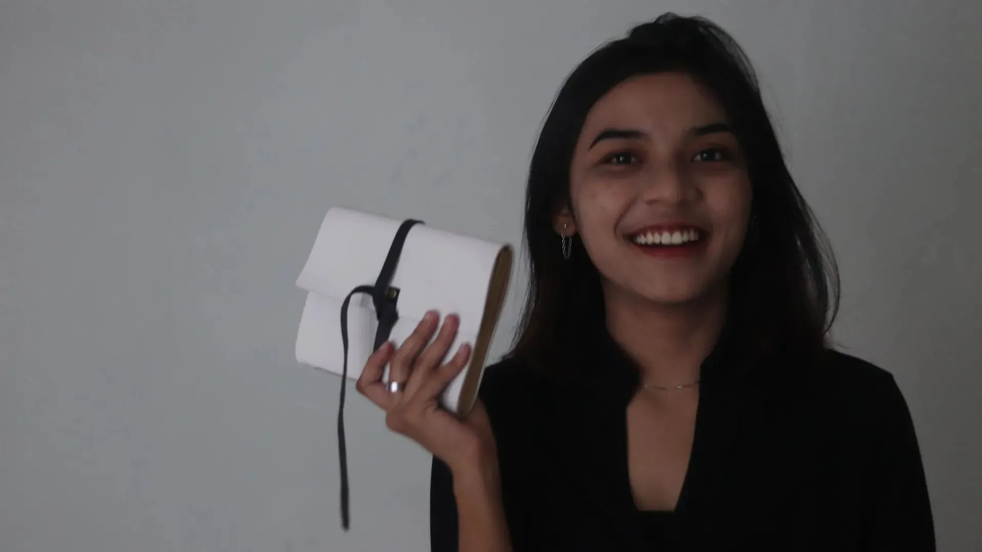 A woman smiles while holding a white notebook closed with a knotted black leather wraparound strap
