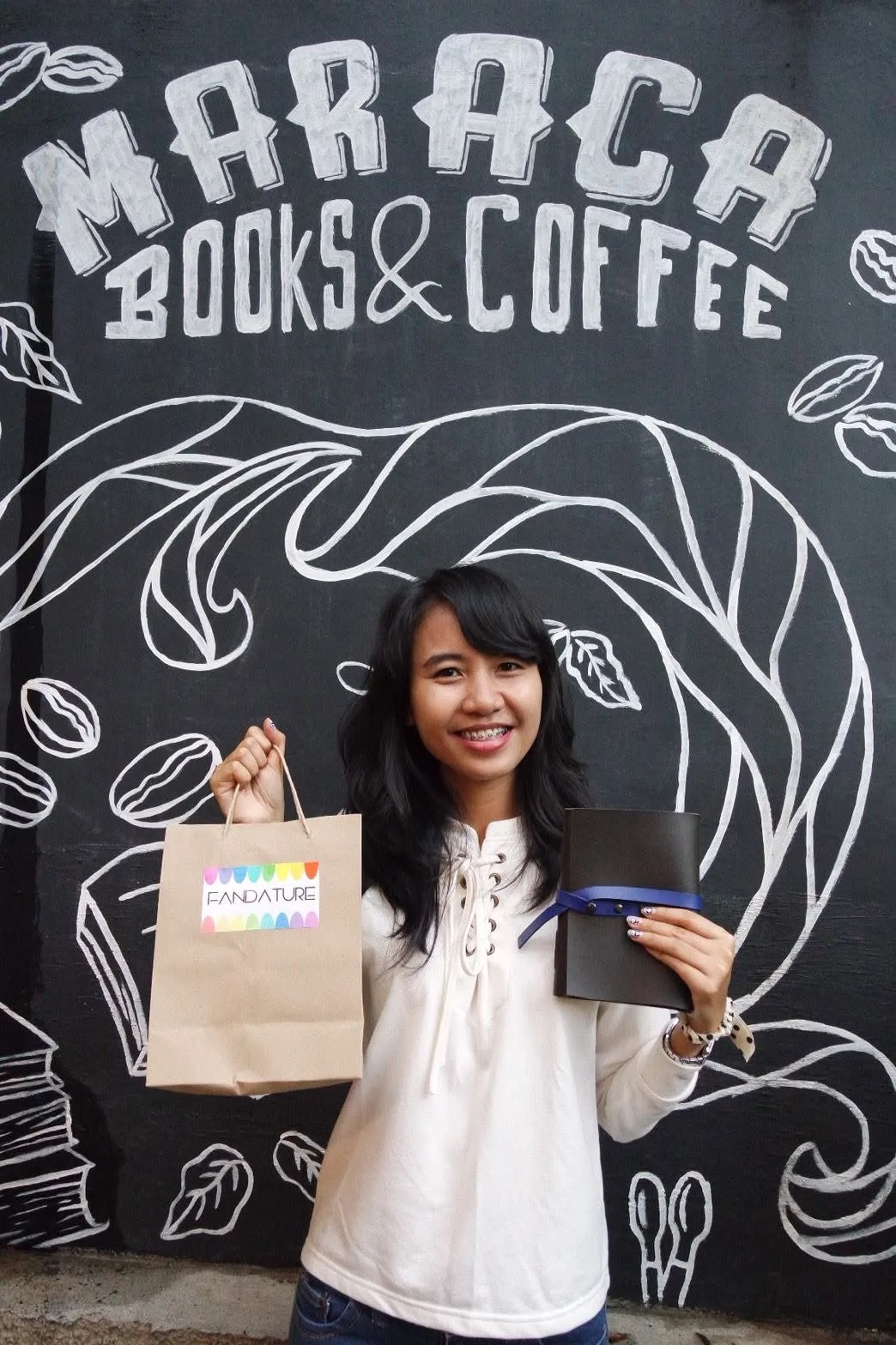 Peserta memegang jurnal kulit buatannya sendiri di depan mural Maraca Books & Coffee