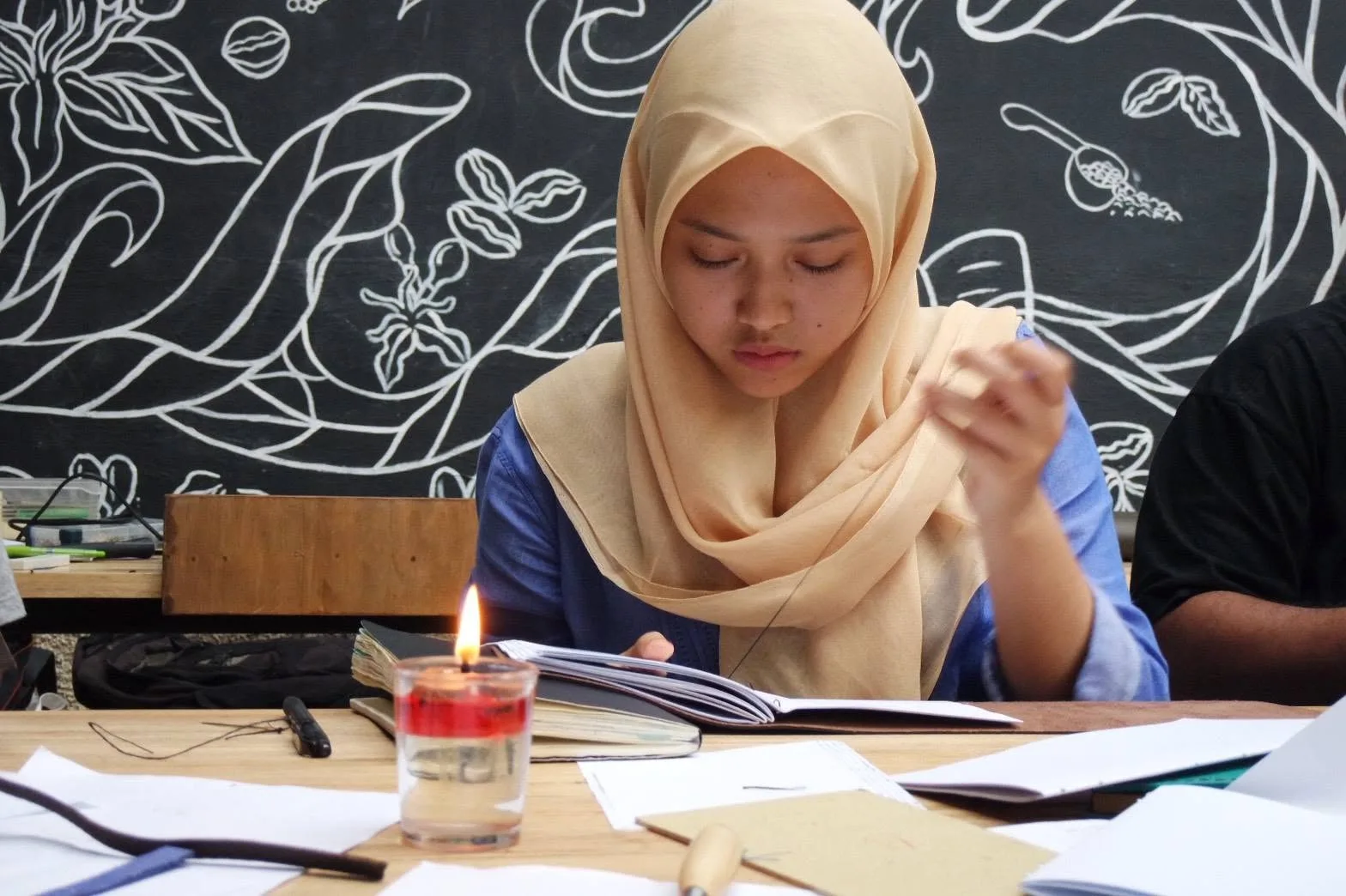Peserta memasang benang ke jarum, dengan lilin untuk melilin benang di meja kerja