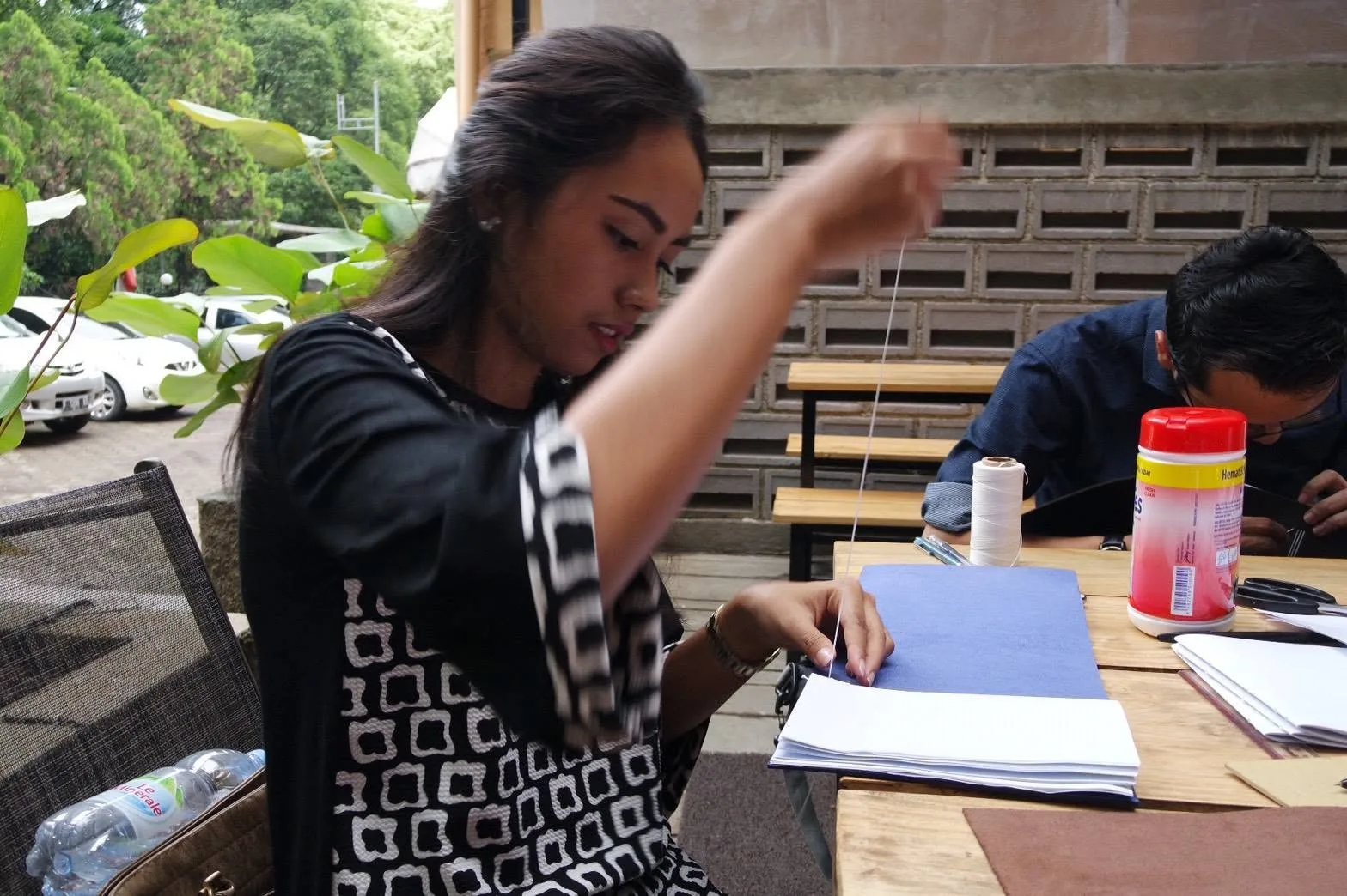 Peserta menarik benang lilin melalui lipatan kertas saat menjahit bukunya