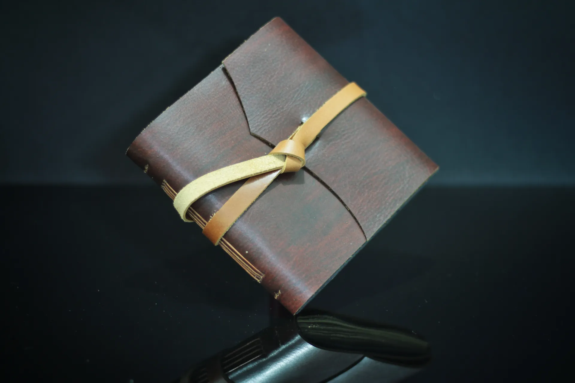 A dark brown leather planner with a tan leather tie, photographed against a dark background