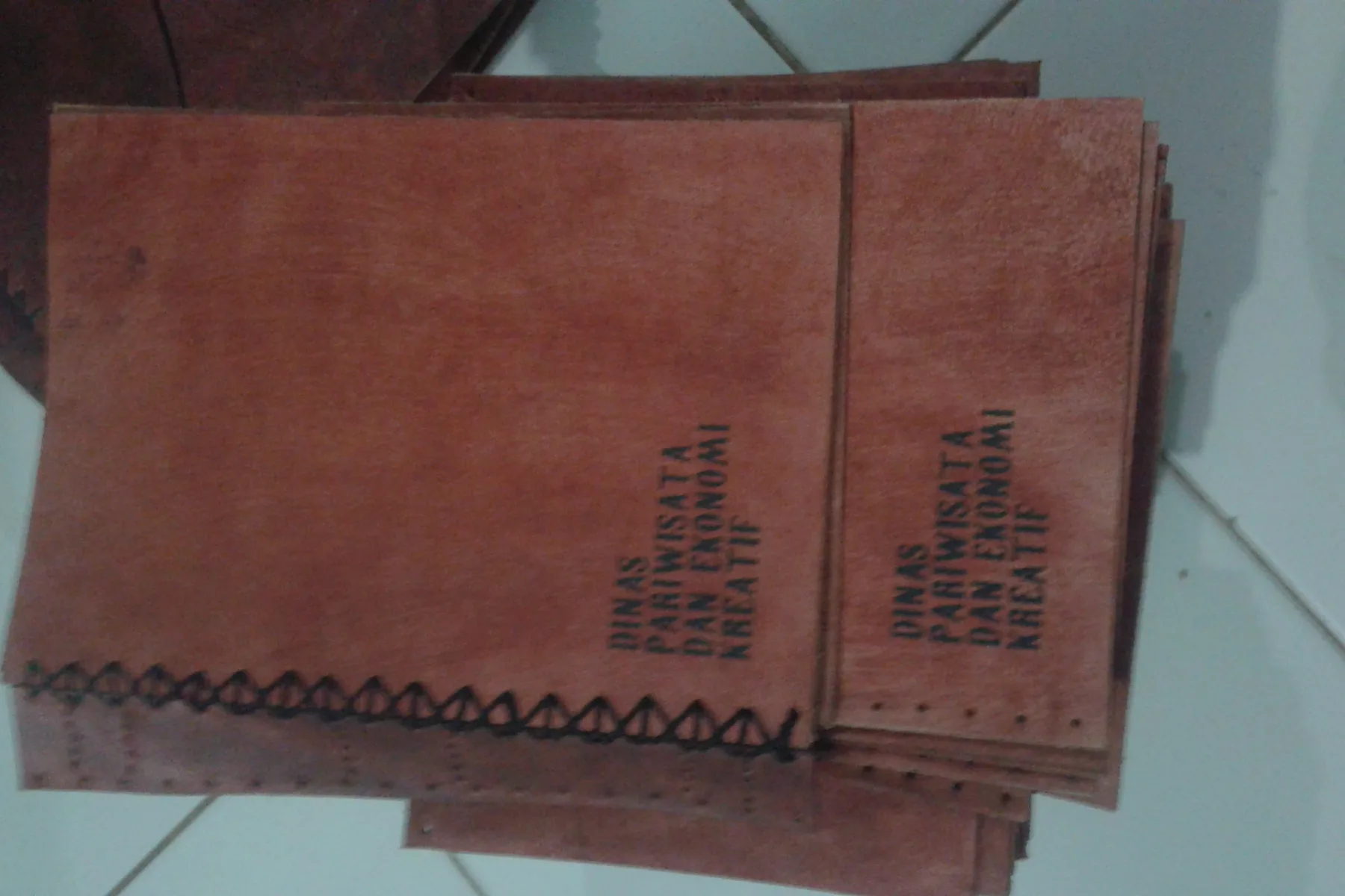 Nama instansi didebos pada sampul kulit cokelat dengan jahitan terbuka di punggung