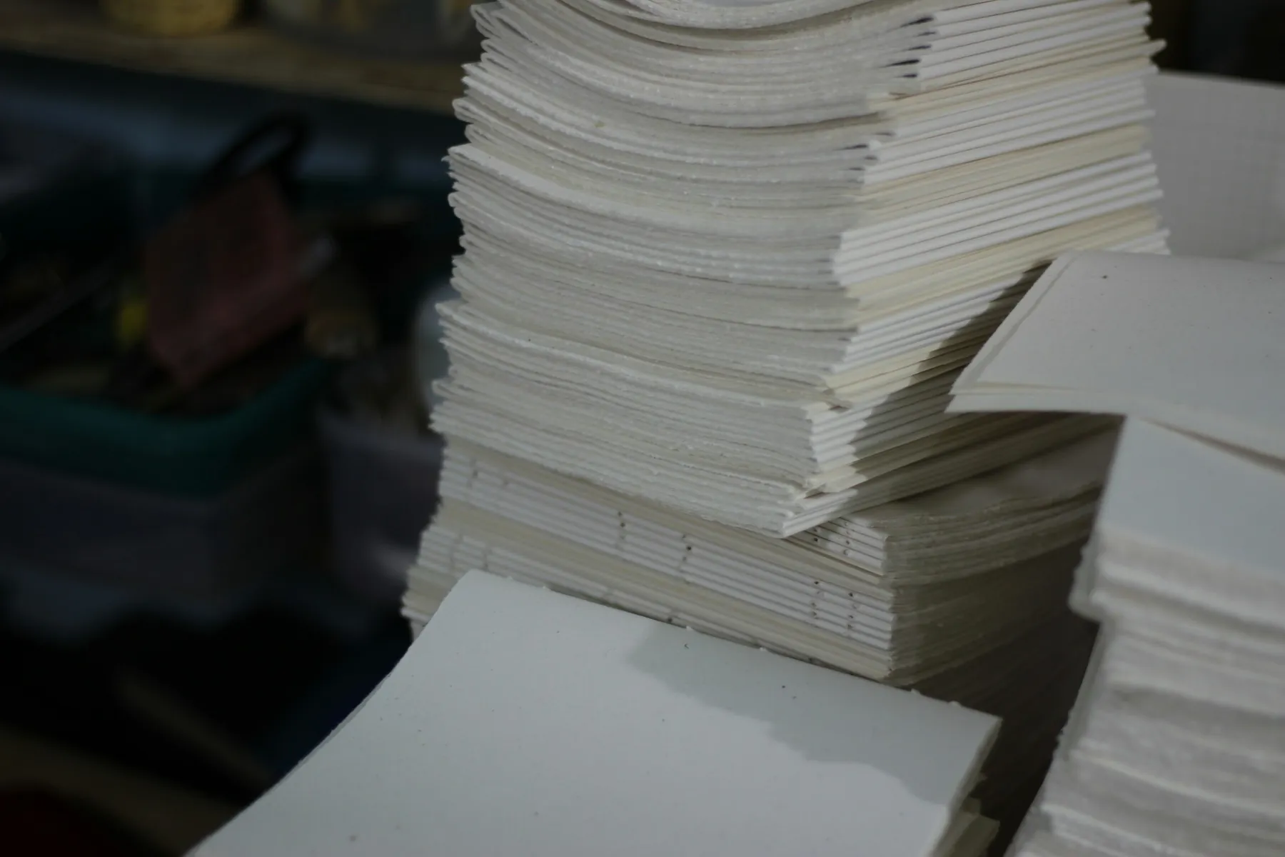 A stack of folded signatures ready for binding, with one already-sewn text block beneath them