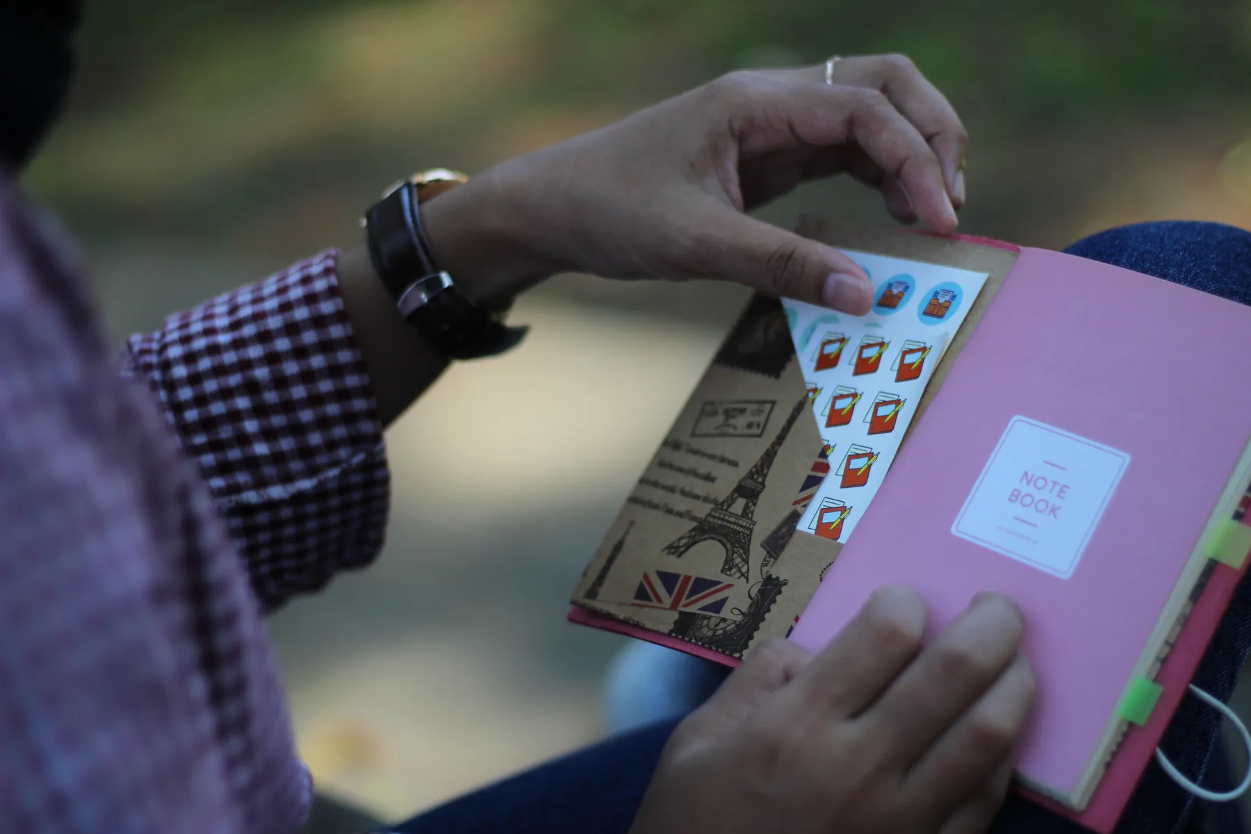 Hands sticking a sheet of stickers into a pink-covered Hibrkraft notebook holding a patterned paper pocket