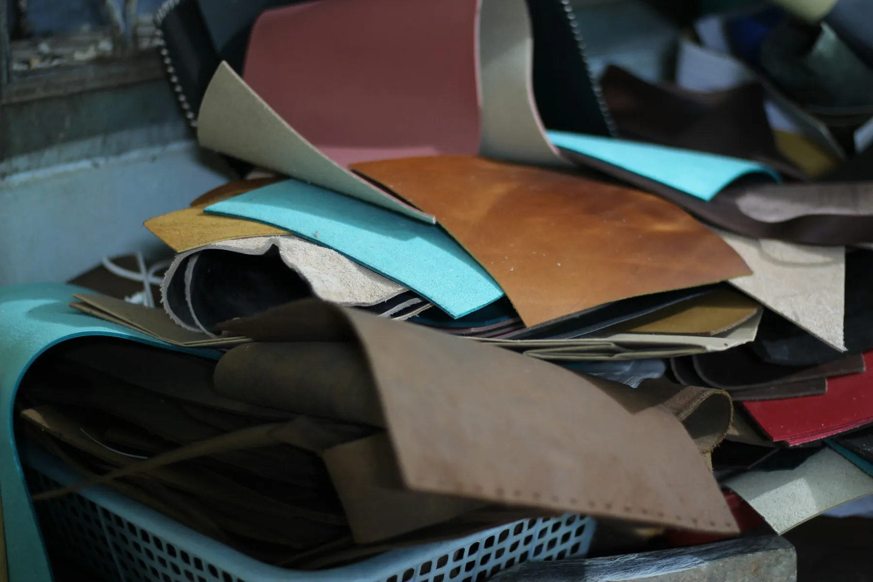 A basket of leather offcuts in various colours and tannages: pink, teal, brown, cream, yellow and red