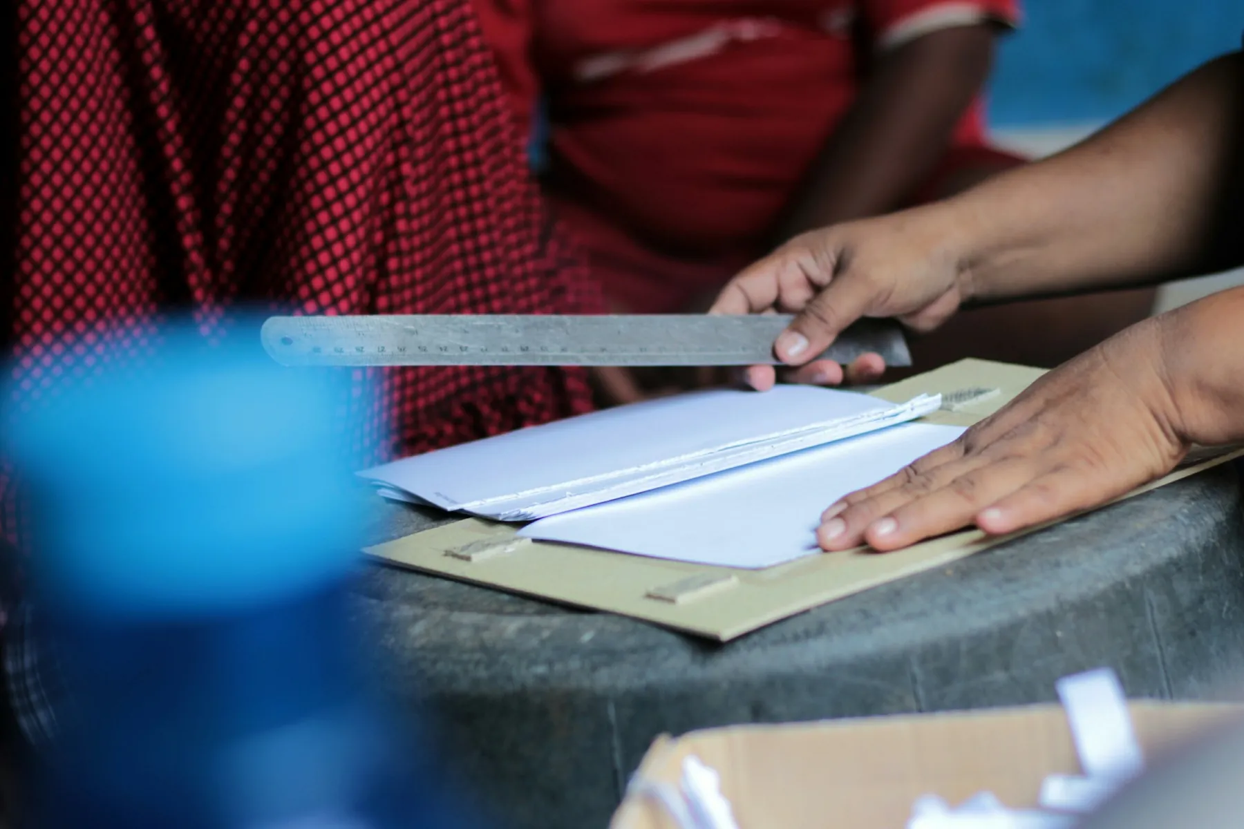 Two people measuring and folding sheets of paper with a metal rule at the bench