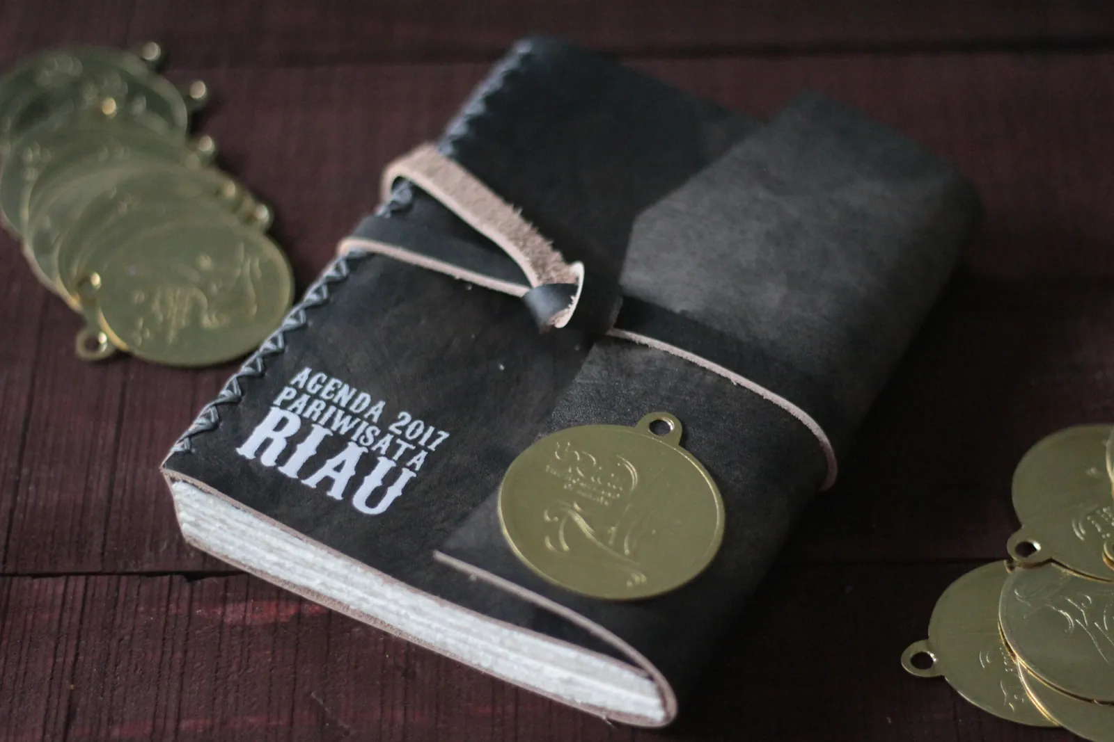 A black leather planner lettered Agenda 2017 Pariwisata Riau, with a brass charm