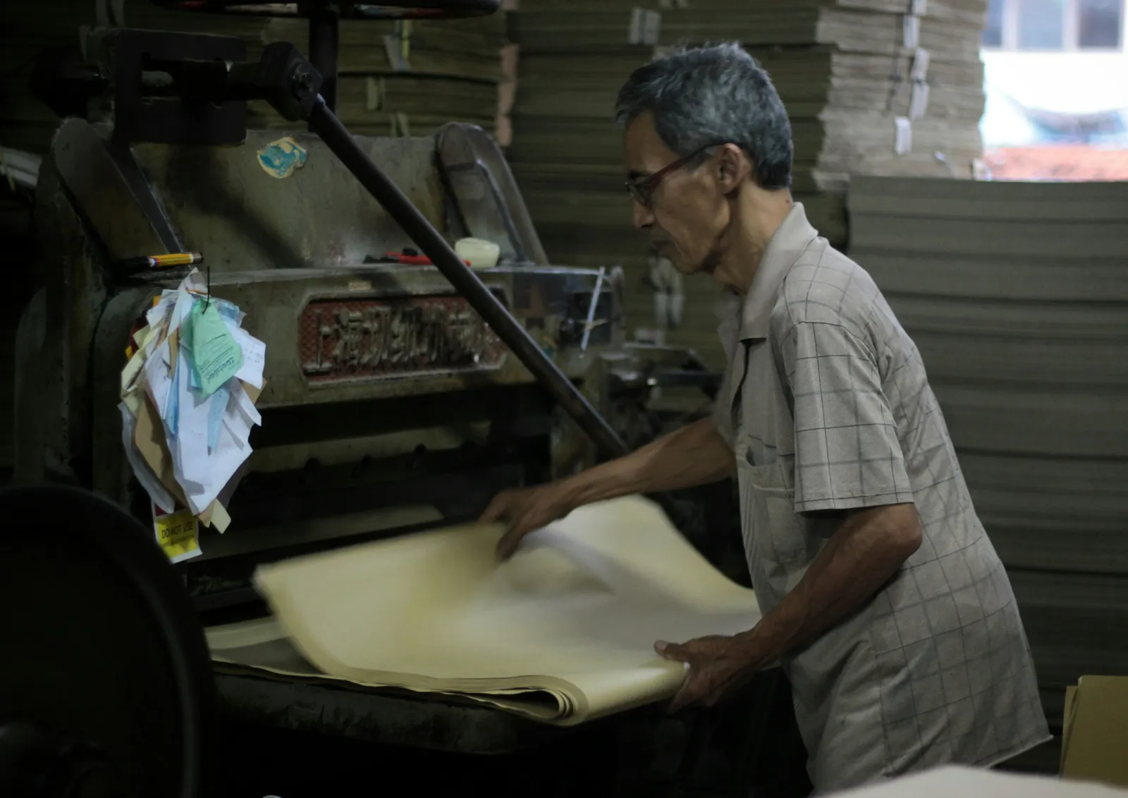 A man operating an industrial paper-cutting machine in front of stacked board
