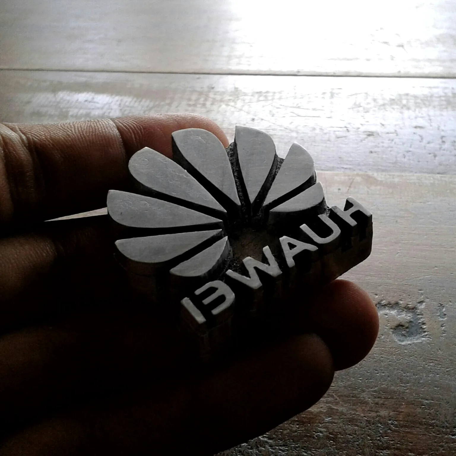 Pelat logam untuk deboss logo dipegang di tangan, di atas meja kerja kayu
