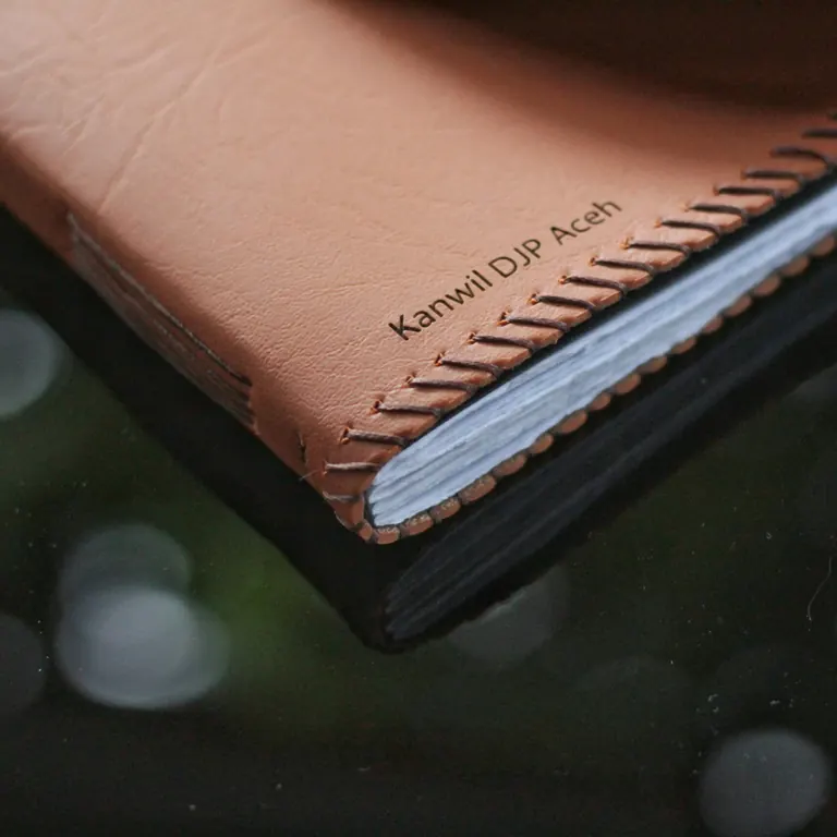 Sudut notebook kulit cokelat dengan jahitan tangan, nama Kanwil DJP Aceh didebos pada kulitnya