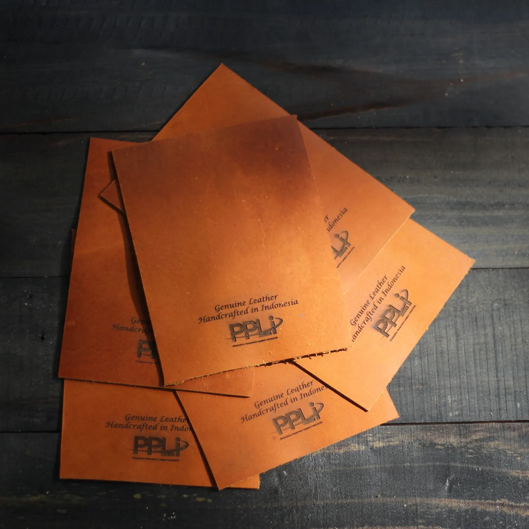 Several loose leather panels laid flat, each debossed with a client logo and the words Genuine Leather, Handcrafted in Indonesia