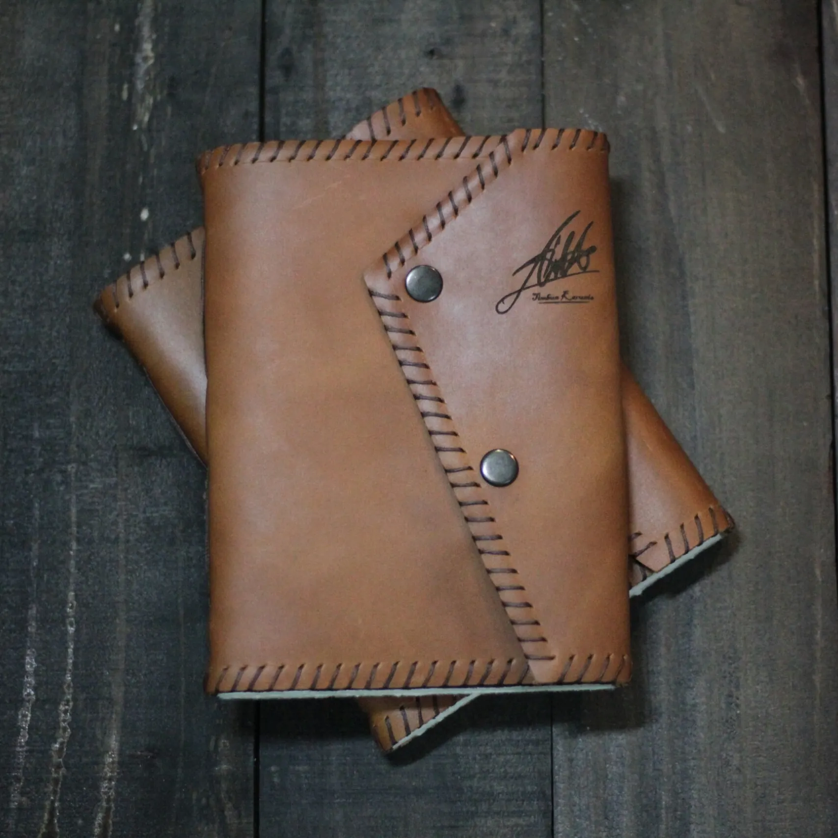 Two whipstitched tan leather folios with snap closures, one debossed with a personal signature near the spine edge